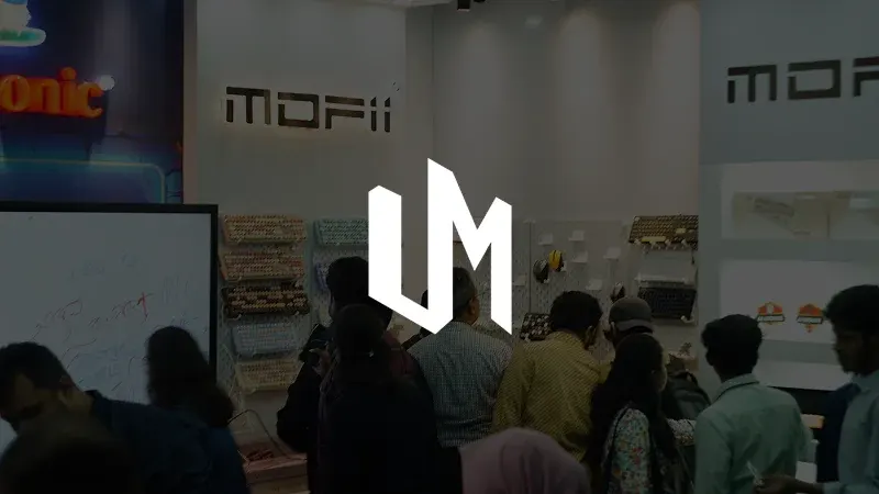 The Unique Modz logo over a photo of their booth at a tech fair, with keyboards on the wall and a crowd in front.