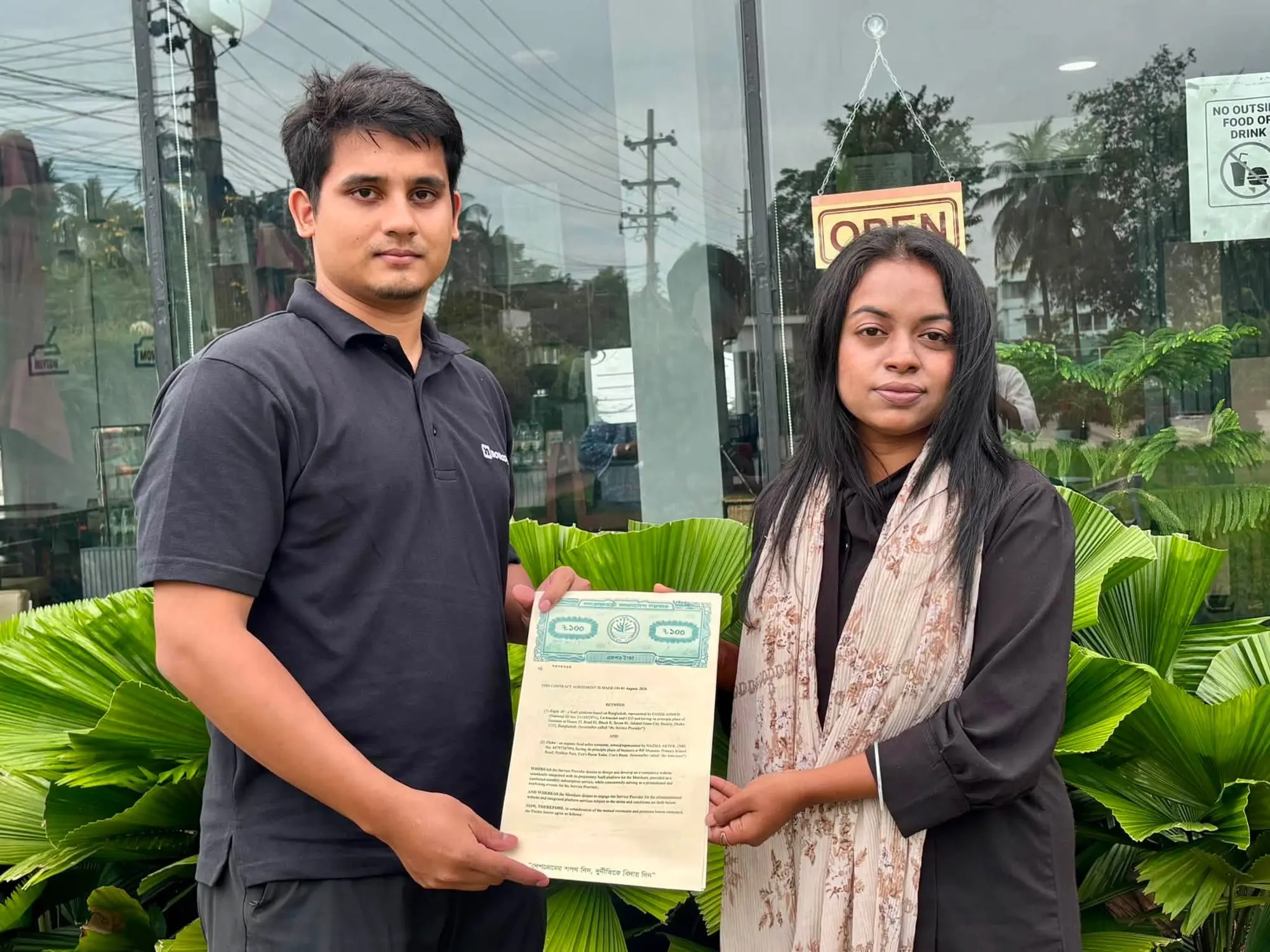 A member of the Zagle team and the merchant's representative outside the shop's cafe in Cox's Bazar, holding up the signed agreement between them.