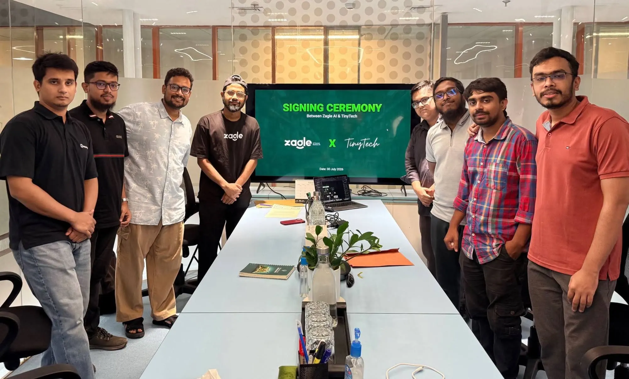 The Zagle and TinyTech teams standing round a meeting table, in front of a screen that reads Signing Ceremony between Zagle AI and TinyTech, 30 July 2026.